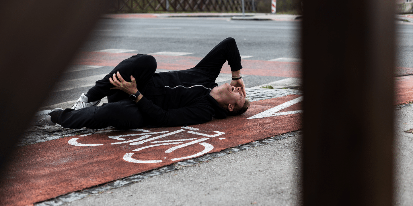 A man lying on the ground holding his knee after being hit by a car